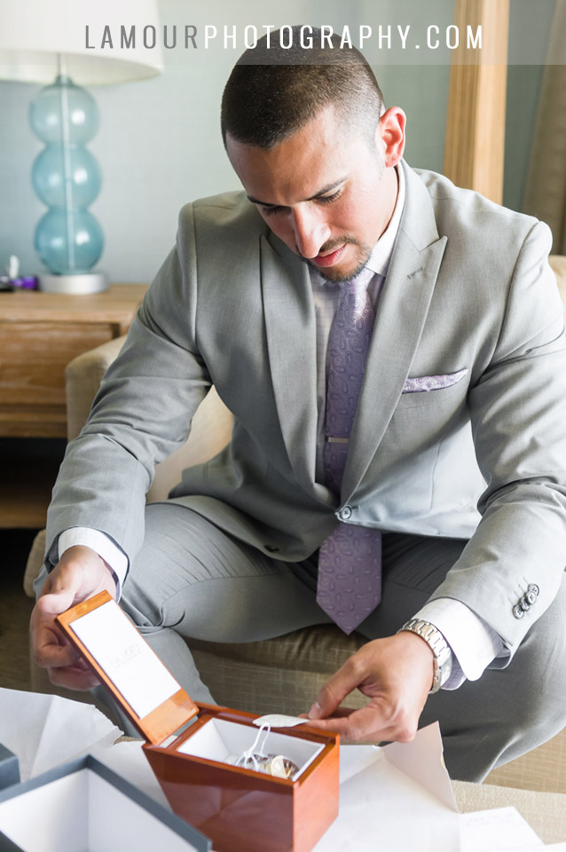 Destination wedding in Hawaii groom in grey suit with lavender tie opening up a gift on his wedding day on Oahu