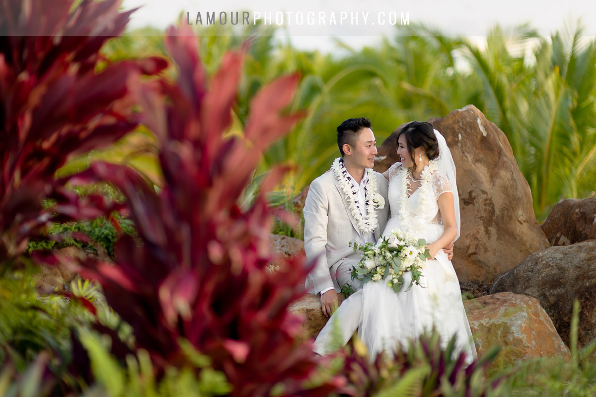 Hawaii bride and groom sit on lava rocks during wedding photography session and video in maui