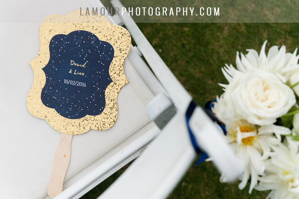 Destination wedding in hawaii had fans for guests during outdoor wedding ceremony with glitter gold outline, navy blue with stars and constellations.