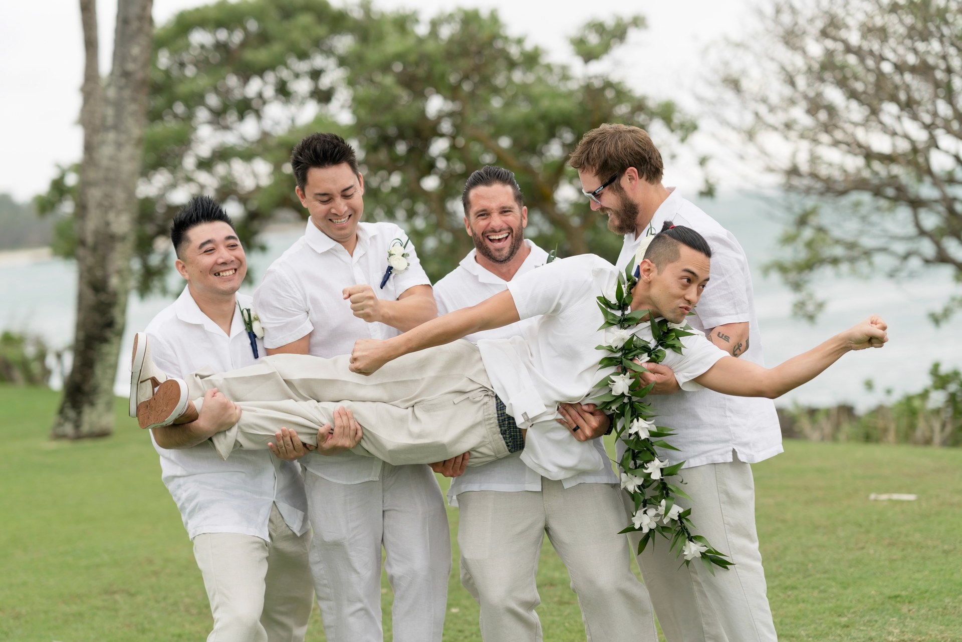 Wedding party laughing as friends lift the groom