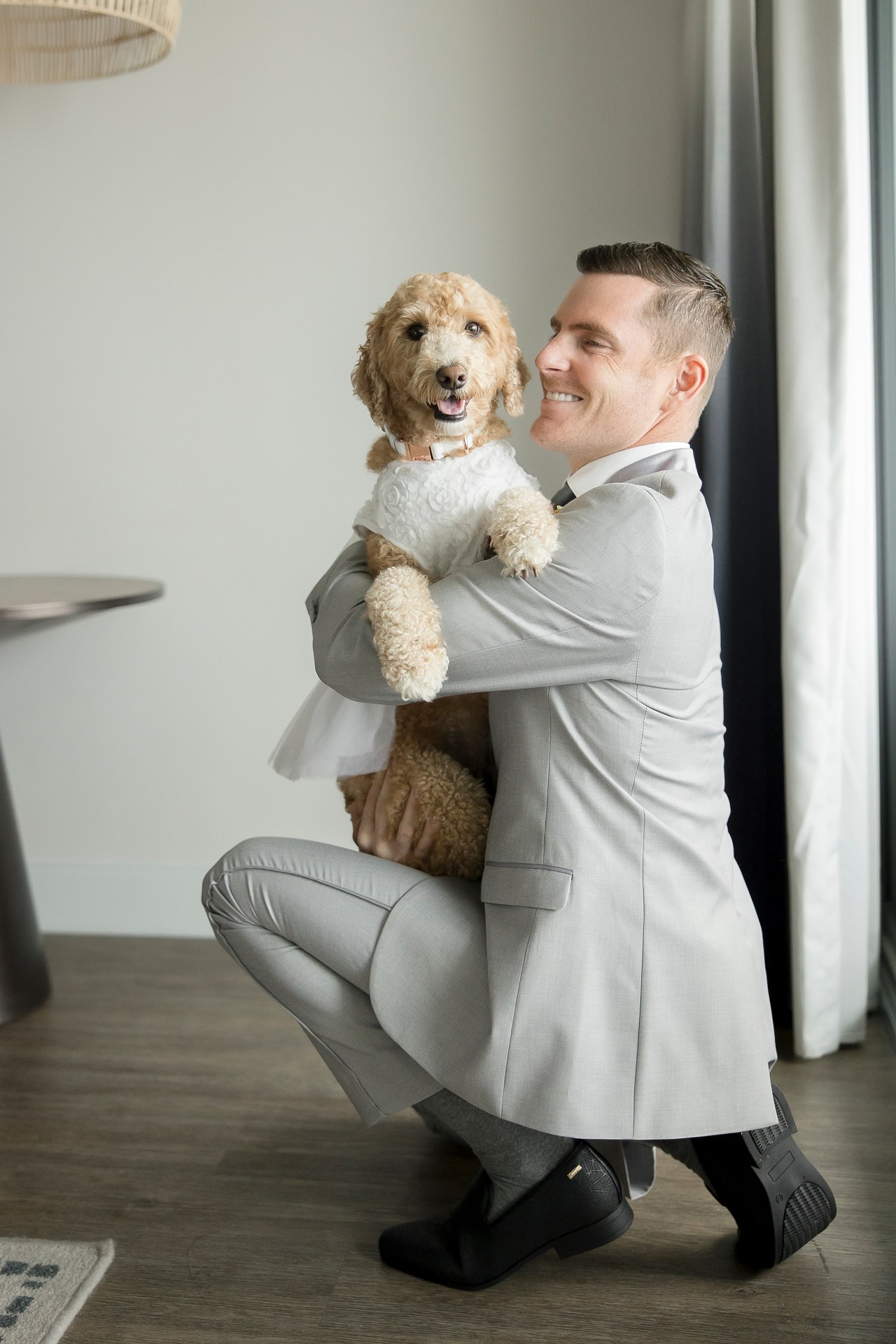A smiling groom holding his dog dressed for the wedding