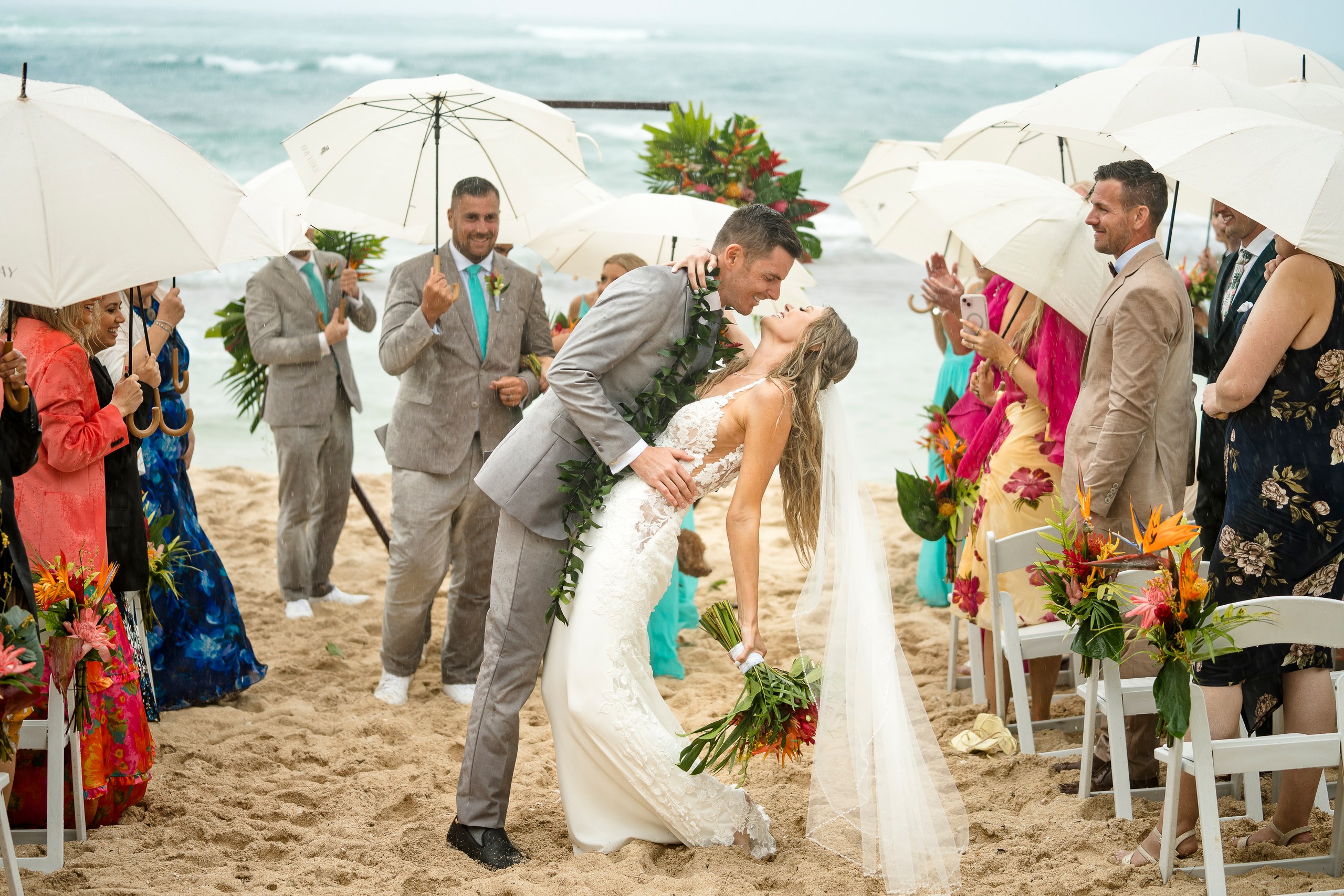 Newlyweds kissing in the aisle while guests hold white parasols