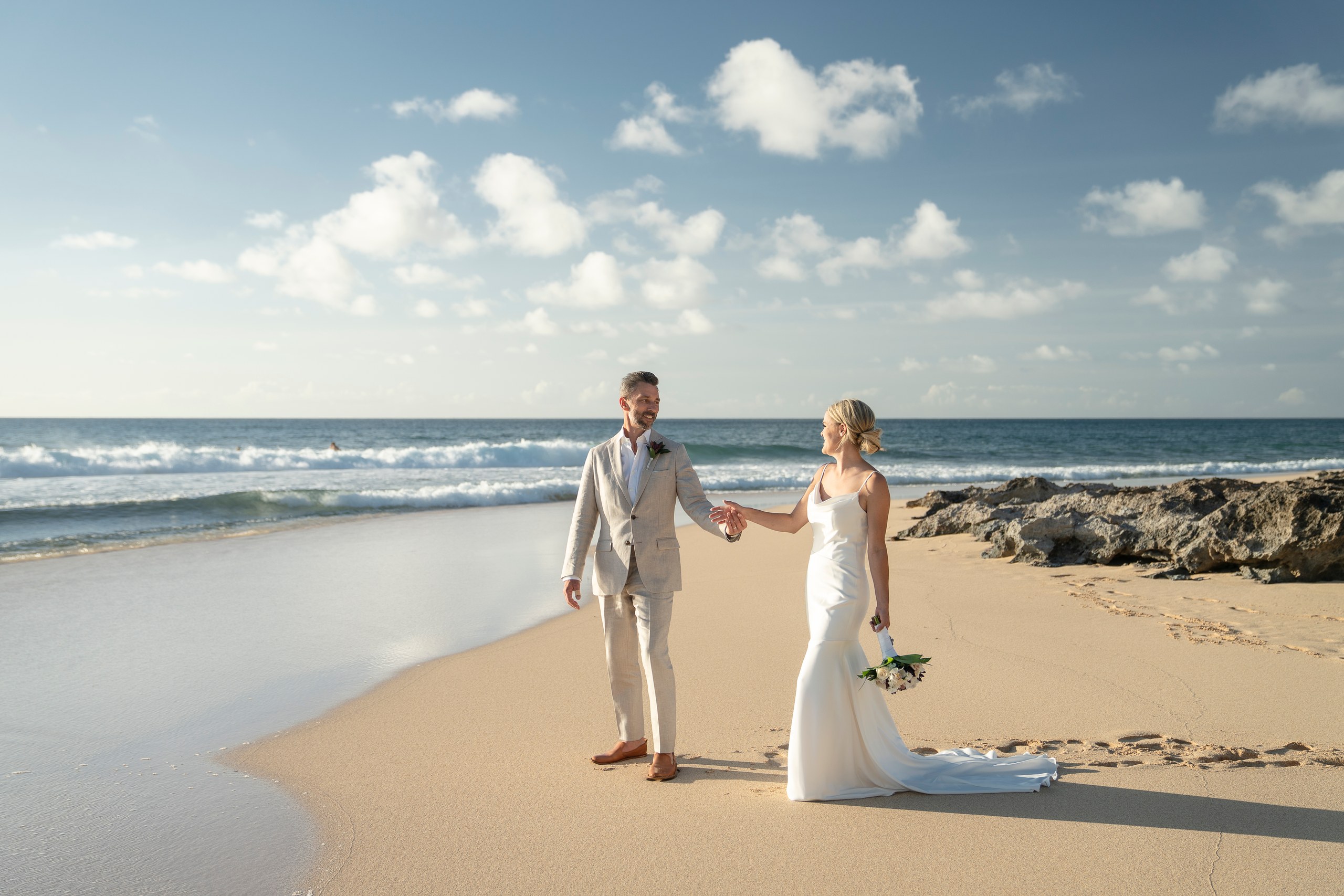 Bride and groom holding hands on the beach beneath a wide sky