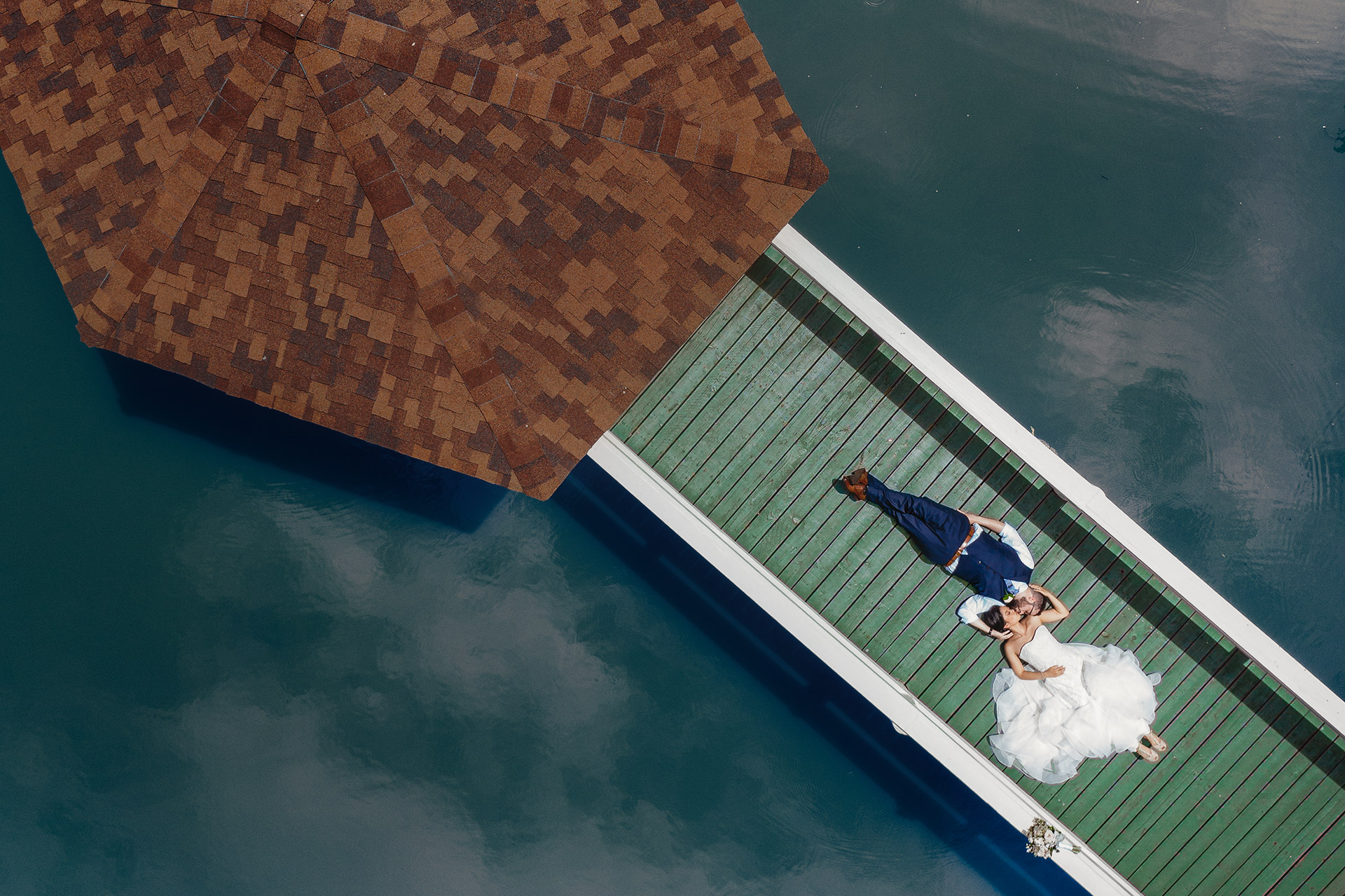 A couple on a dock above the water, photographed from above